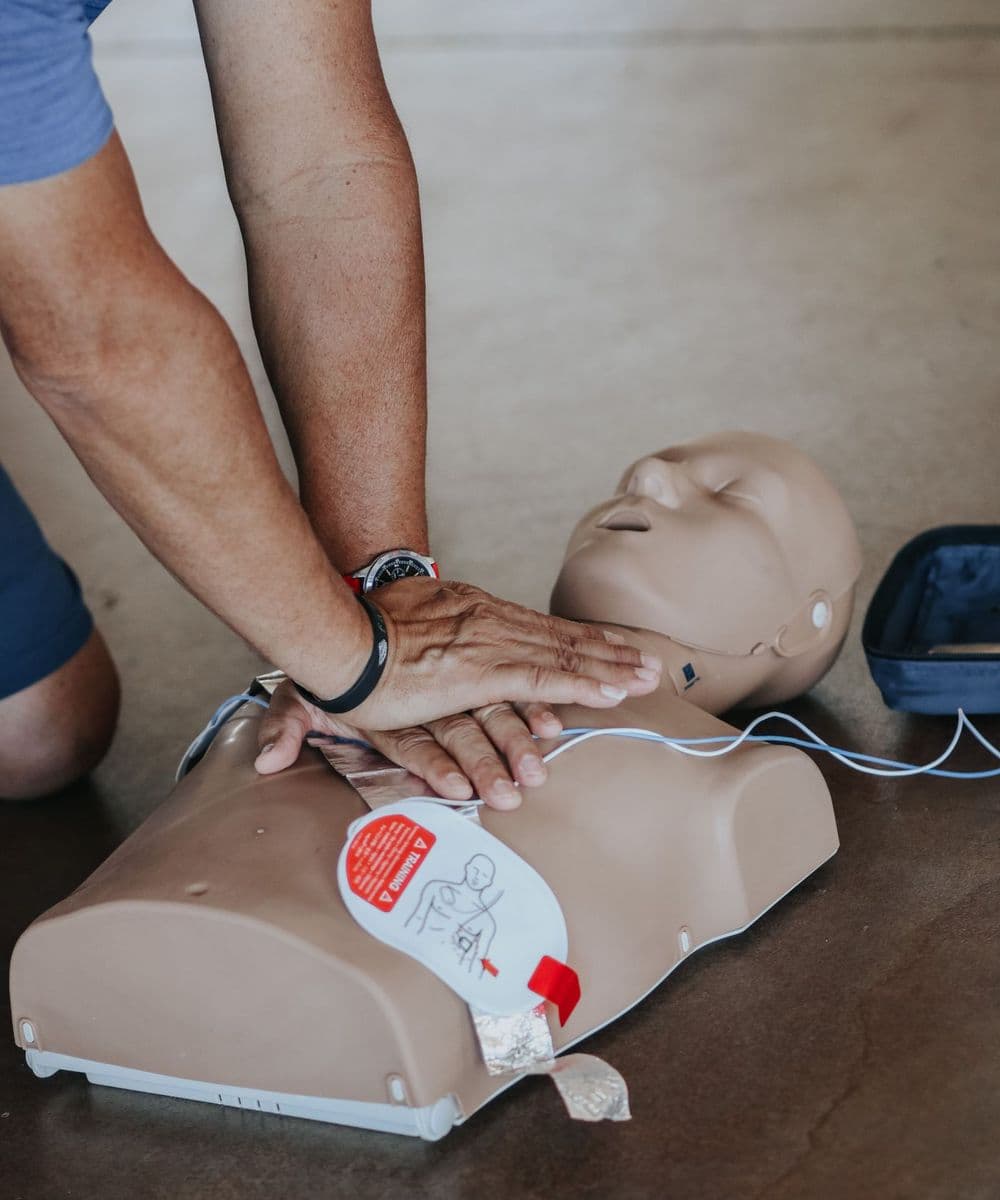 A student practising chest compressions on a manikin with an AED trainer alongside